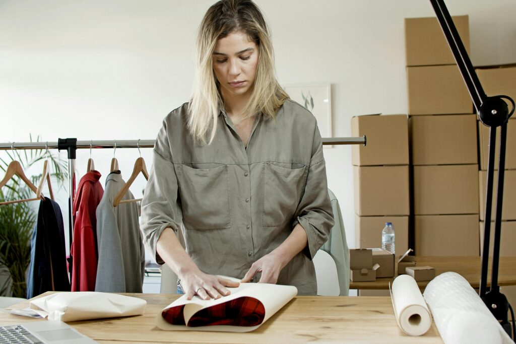 A woman in an office packing clothes with wrapping paper for online store sales.